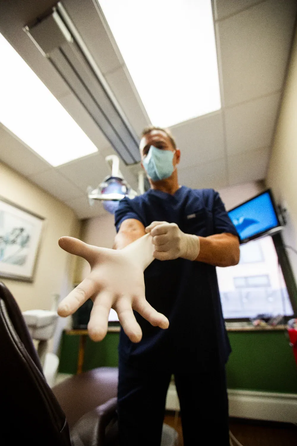 Dentist putting on latex gloves before a procedure in a treatment room at Creative Dentistry of Brooklyn Heights