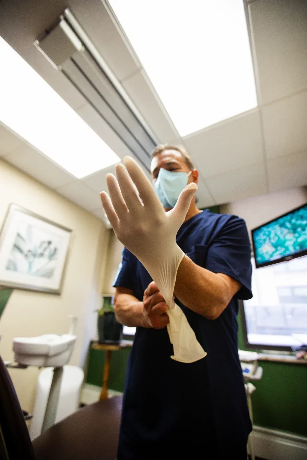 Dentist wearing mask and putting on gloves in dental office